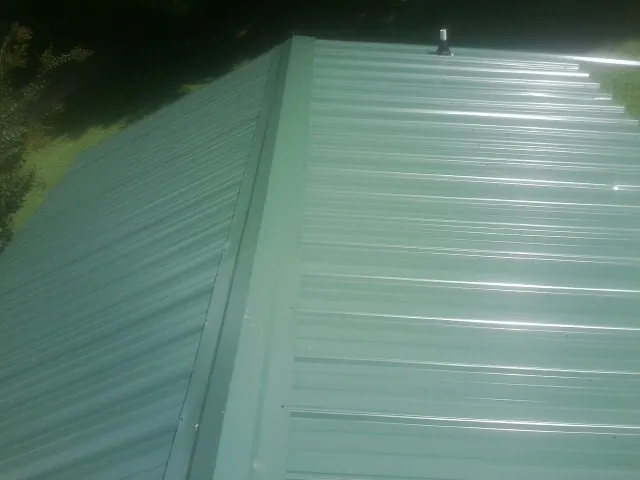 New green metal panels meeting at the ridge of a roof — Flat Roof Repair work by our crew in Brentwood